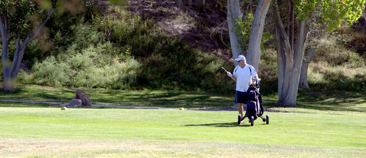 一名男子走在高尔夫球场上，旁边放着一套球杆.