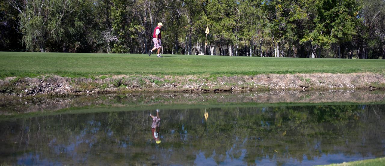 Hero image of man walking towards the golf flag, with a water hazard in the foreground.